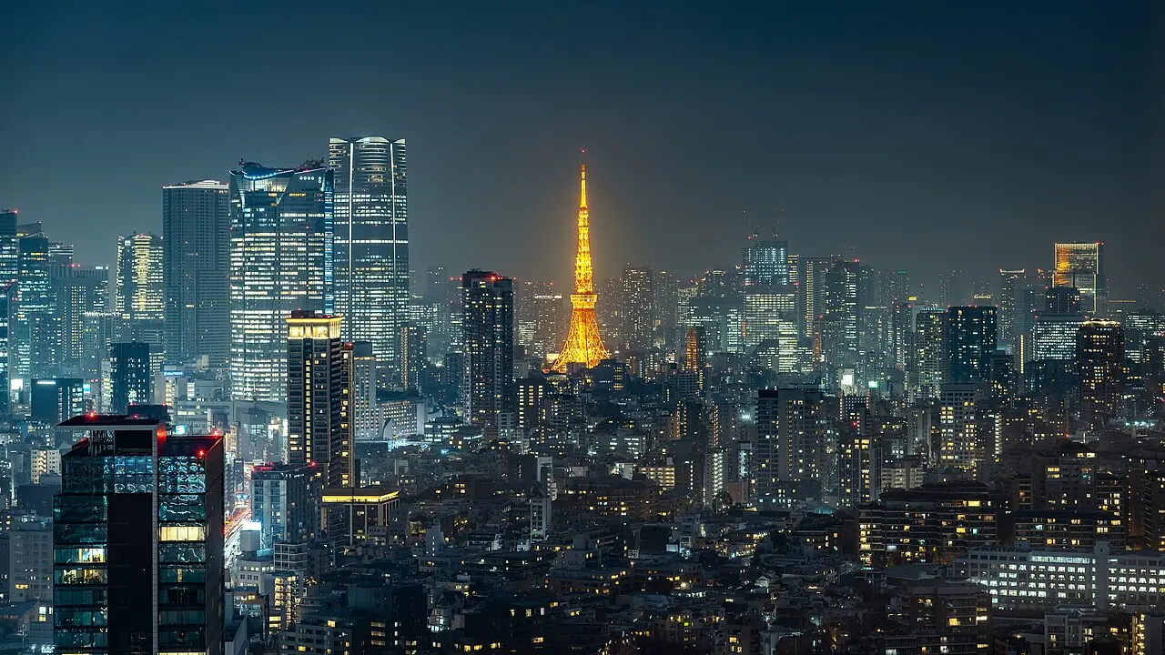 A high-angle night photograph of Tokyo , Japan. The Tokyo Tower is prominently illuminated in its traditional orange "Landmark Light." To th